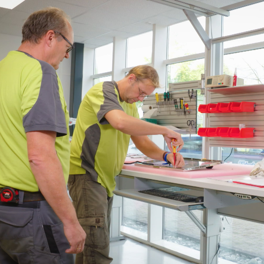 Zwei Menschen stehen in einer Werkstatt und arbeiten.