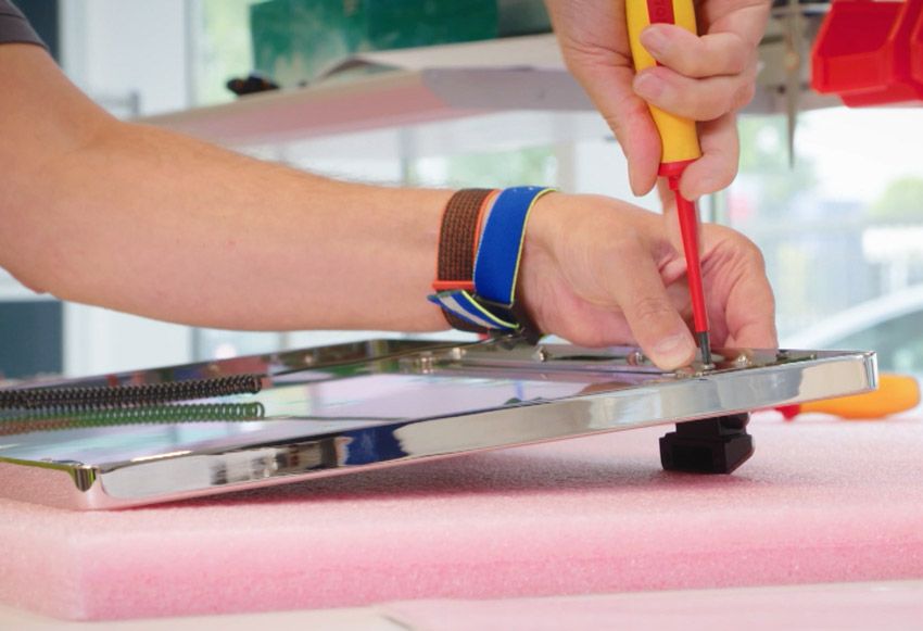 Ein Mensch schraubt Metallteile in einer Werkstatt zusammen.