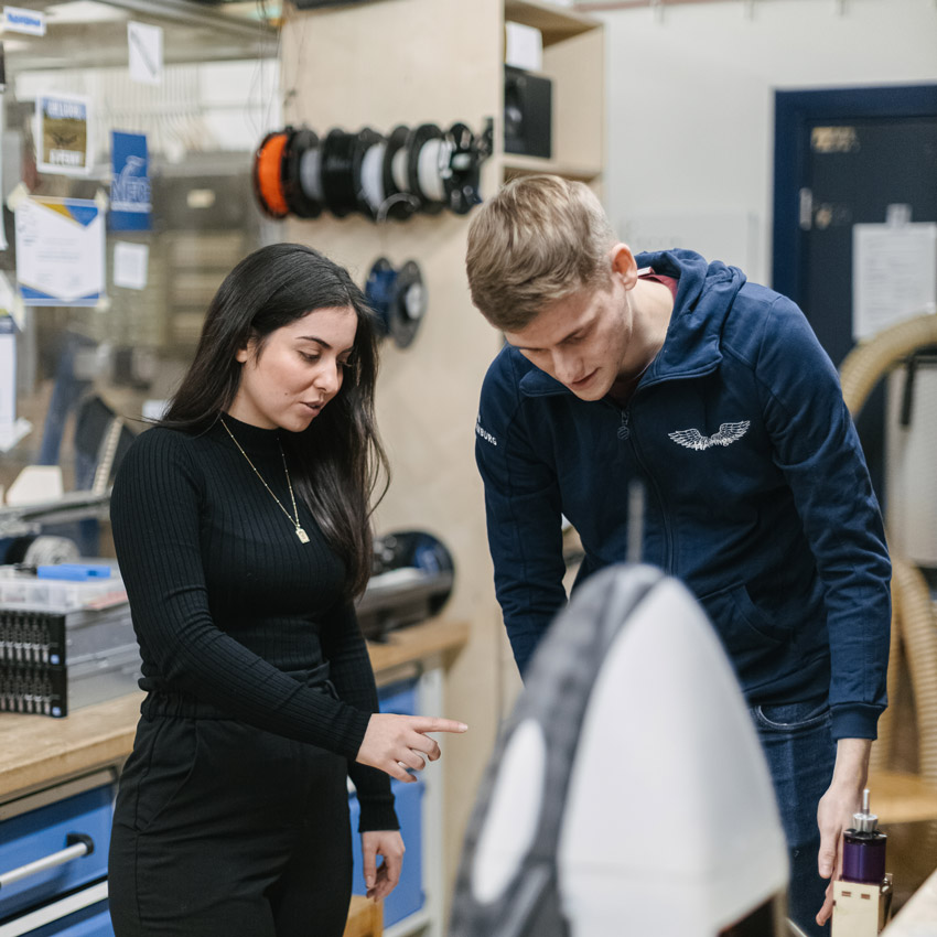 Eine Frau und ein Mnn stehen in einer Werkstatt und besprechen ein Elektronikprojekt.